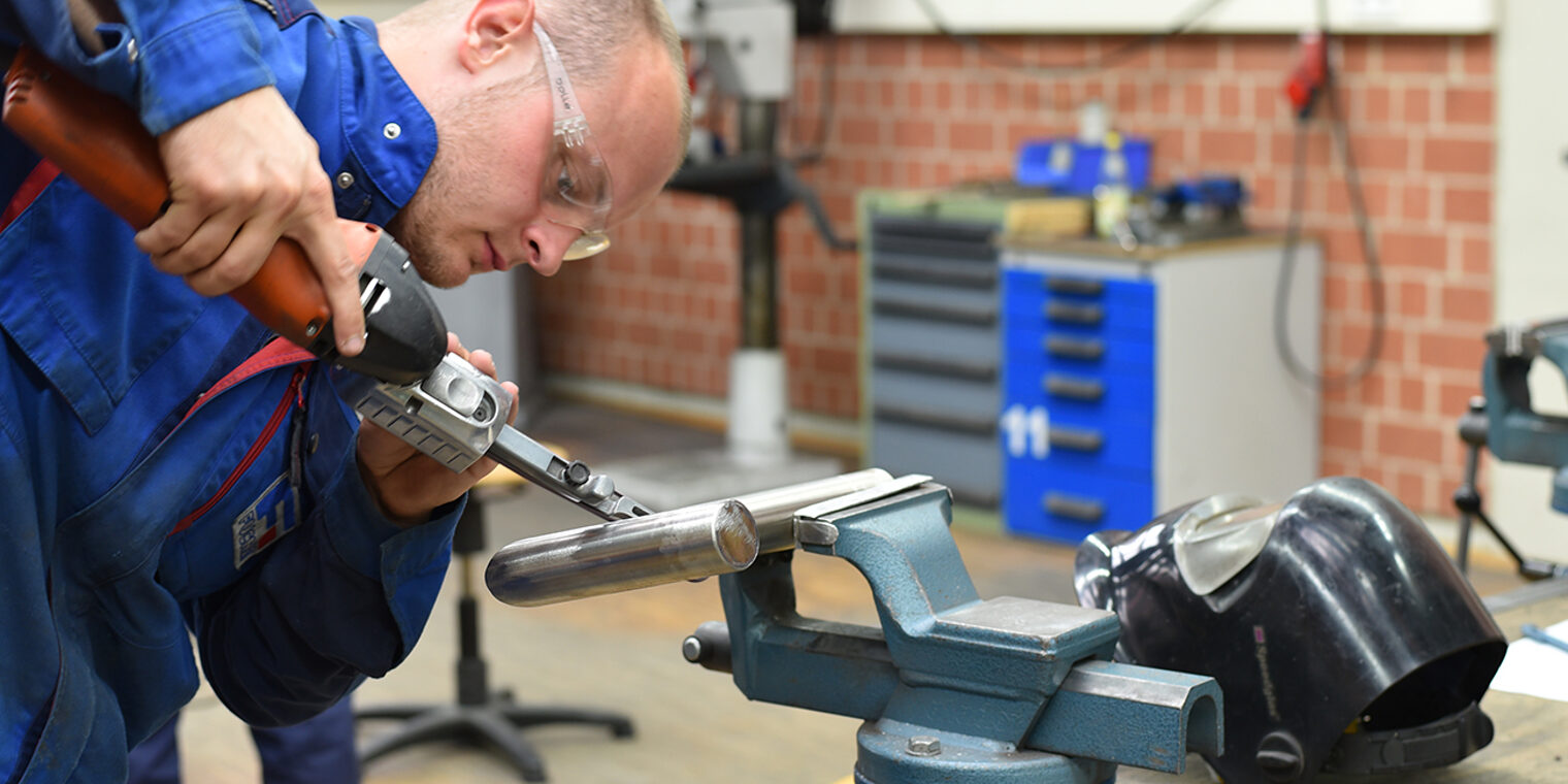 Kursteilnehmer mit Schutzbrille beim Schleifen eines Metallteils