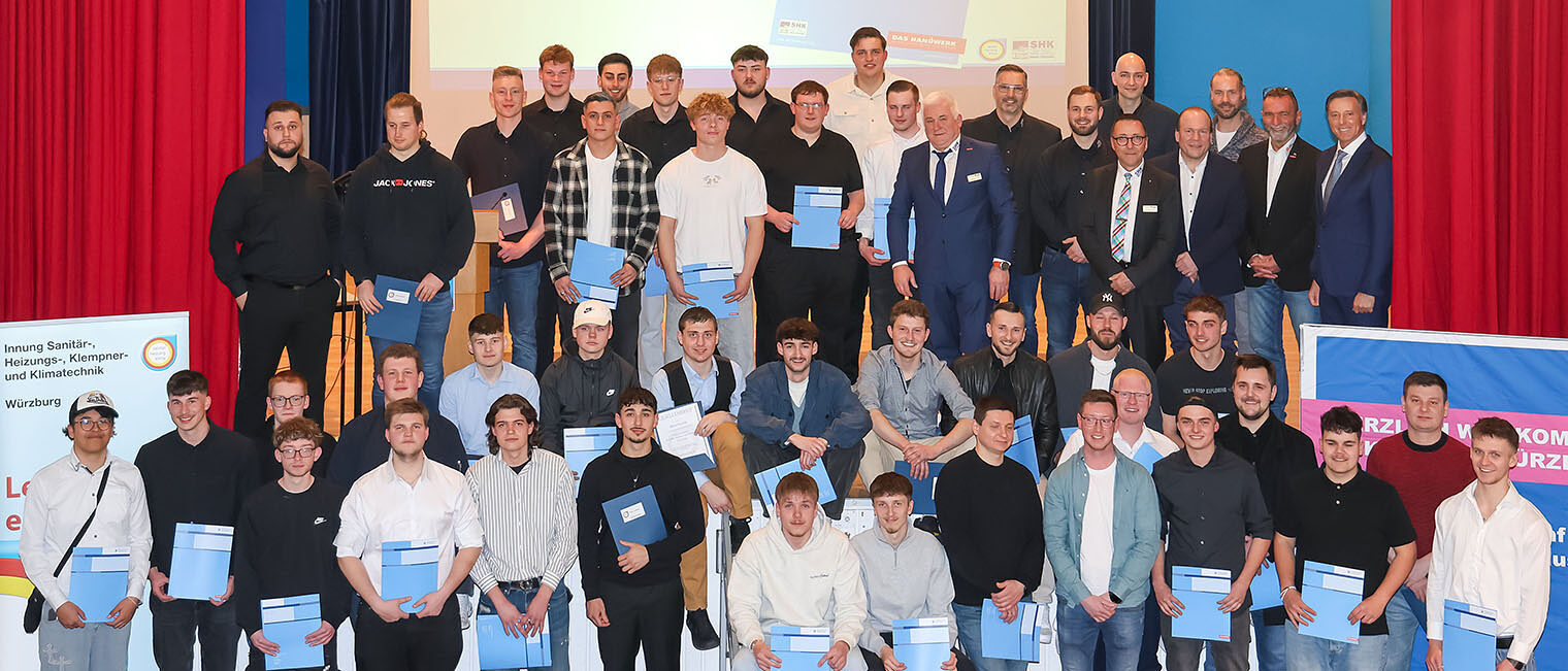 Gruppenbild mit rund 50 Personen auf einer Bühne - Freigesprochene Gesellen der SHK-Innungen mit Zeugnissen in den Händen
