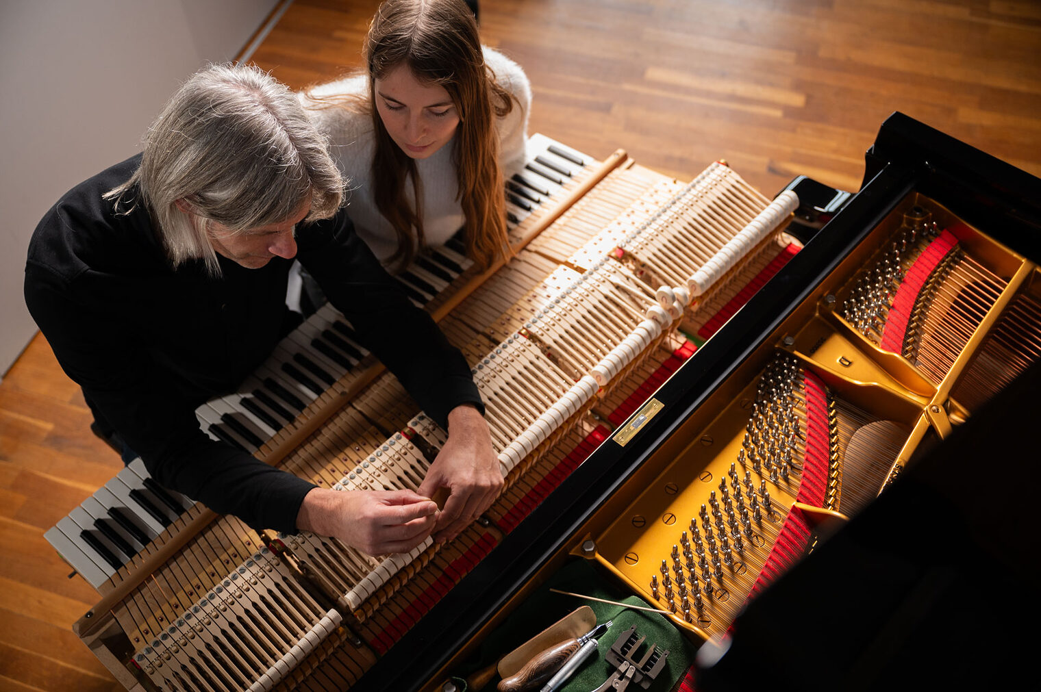 Mann und junge Frau schauen sich Hammerköpfe eines Flügels an Mann und junge Frau schauen sich Hammerköpfe eines Flügels an