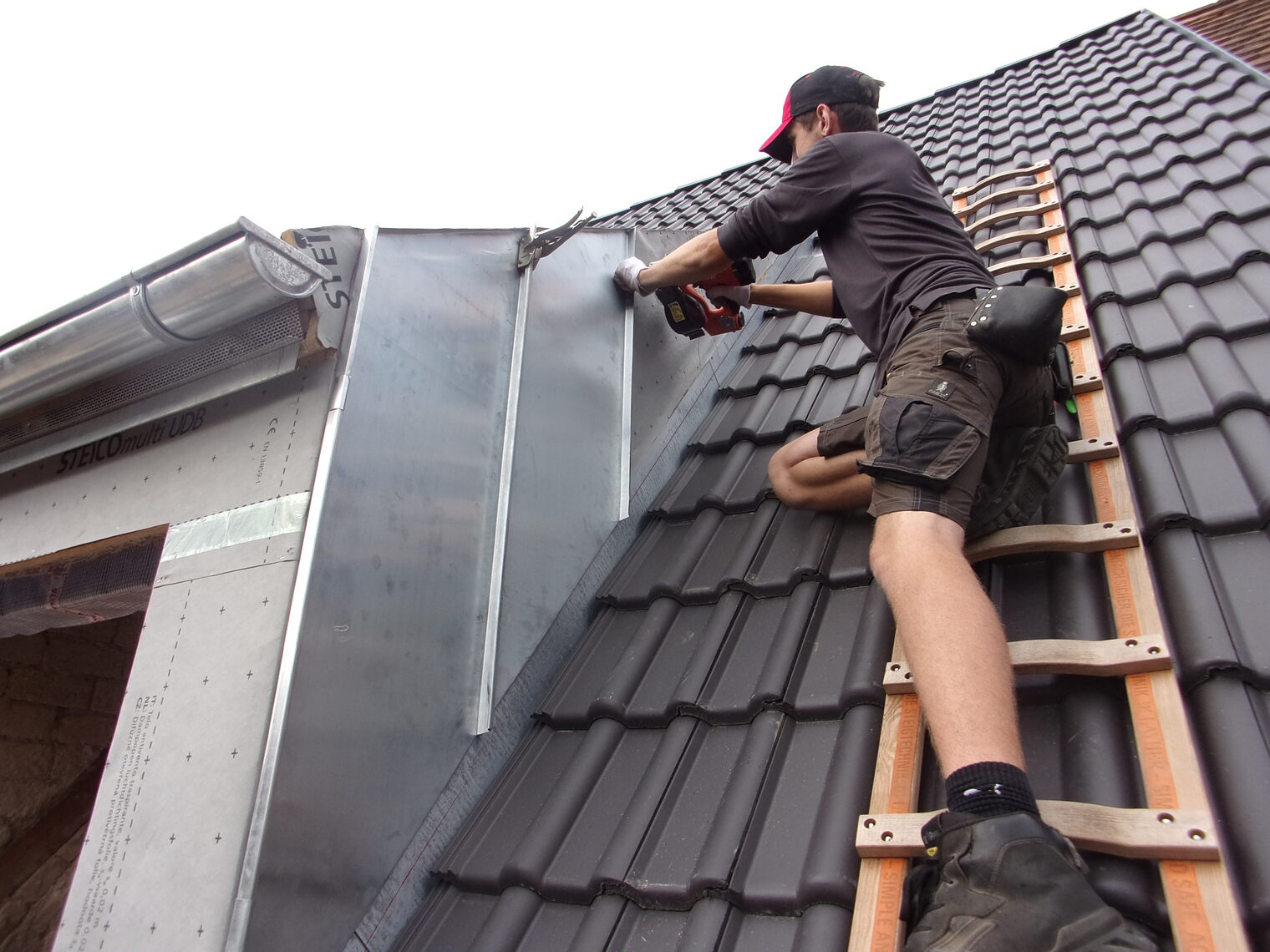 Junger Mann auf Leiter auf Dach arbeitet an Hausfassade Junger Mann auf Leiter auf Dach arbeitet an Hausfassade
