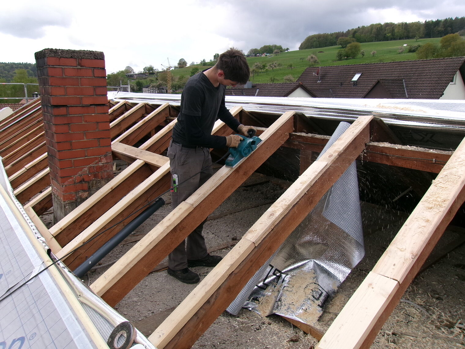 Junger Mann arbeitet im Dachstuhl eines Hauses, Dach ist abgenommen Junger Mann arbeitet im Dachstuhl eines Hauses, Dach ist abgenommen