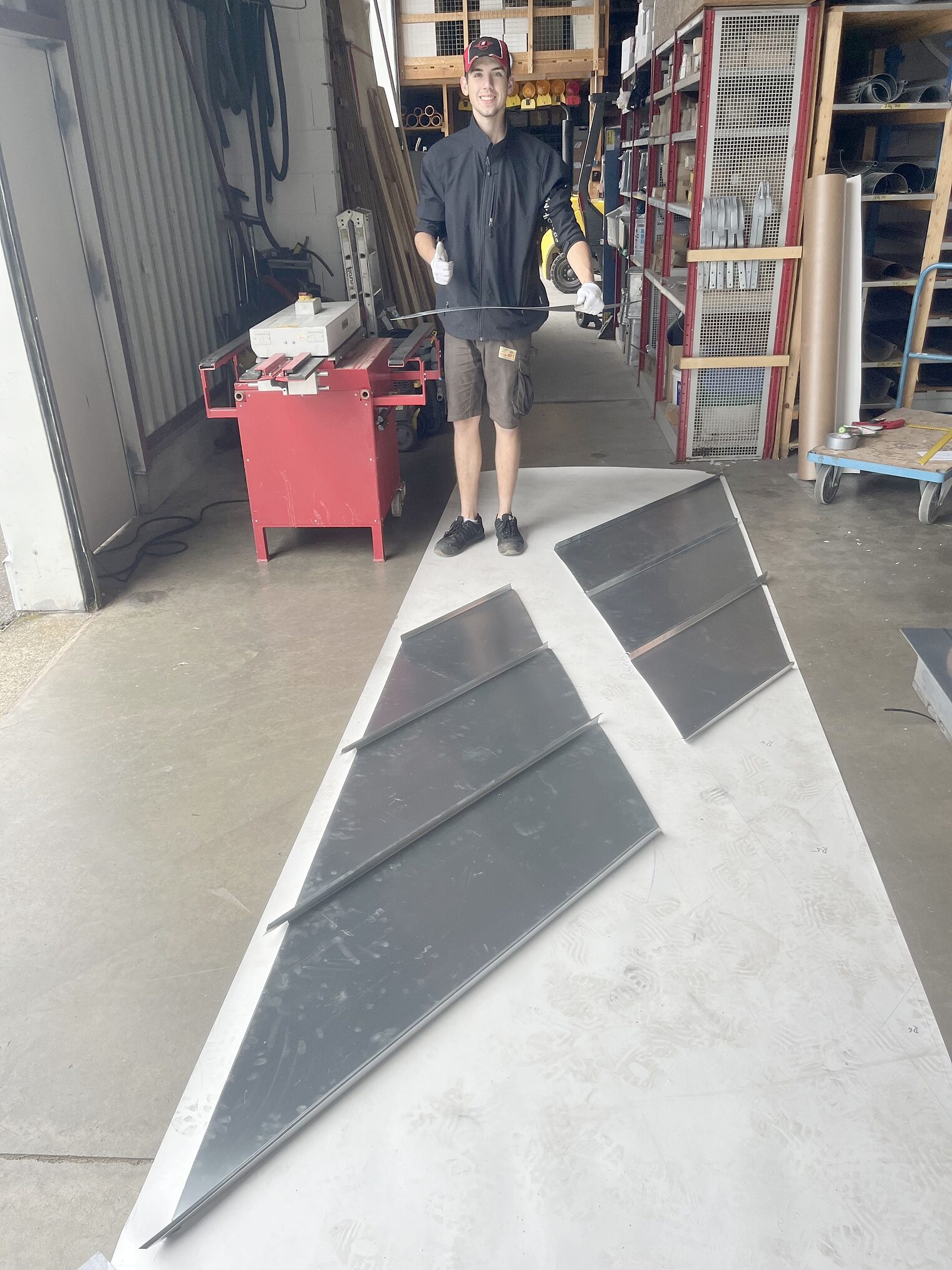 Junger Mann vor flacher Metallkonstruktion, zeigt Daumen nach oben Junger Mann steht vor flacher Metallkonstruktion, zeigt Daumen nach oben