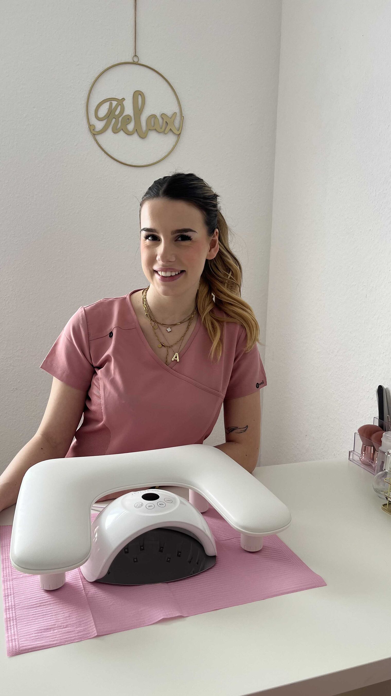 Frau sitz an Tisch mit Nagel-UV-Gerät, lächelt in die Kamera Frau sitz an Tisch mit Nagel-UV-Gerät, lächelt in die Kamera