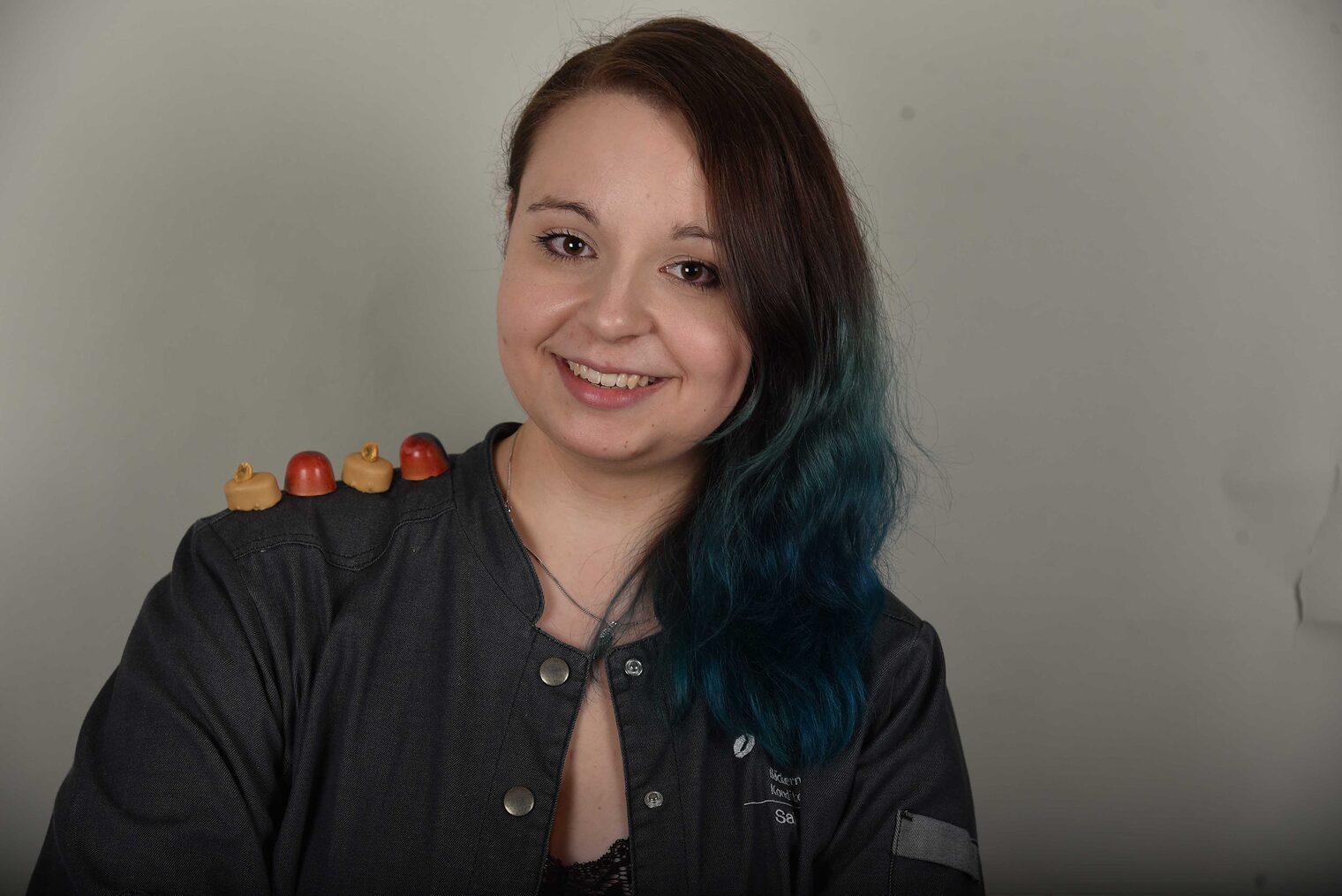 Frau lächelt in die Kamera, 4 Pralinien liegen auf ihrer Schulter Frau lächelt in die Kamera, 4 Pralinien liegen auf ihrer Schulter