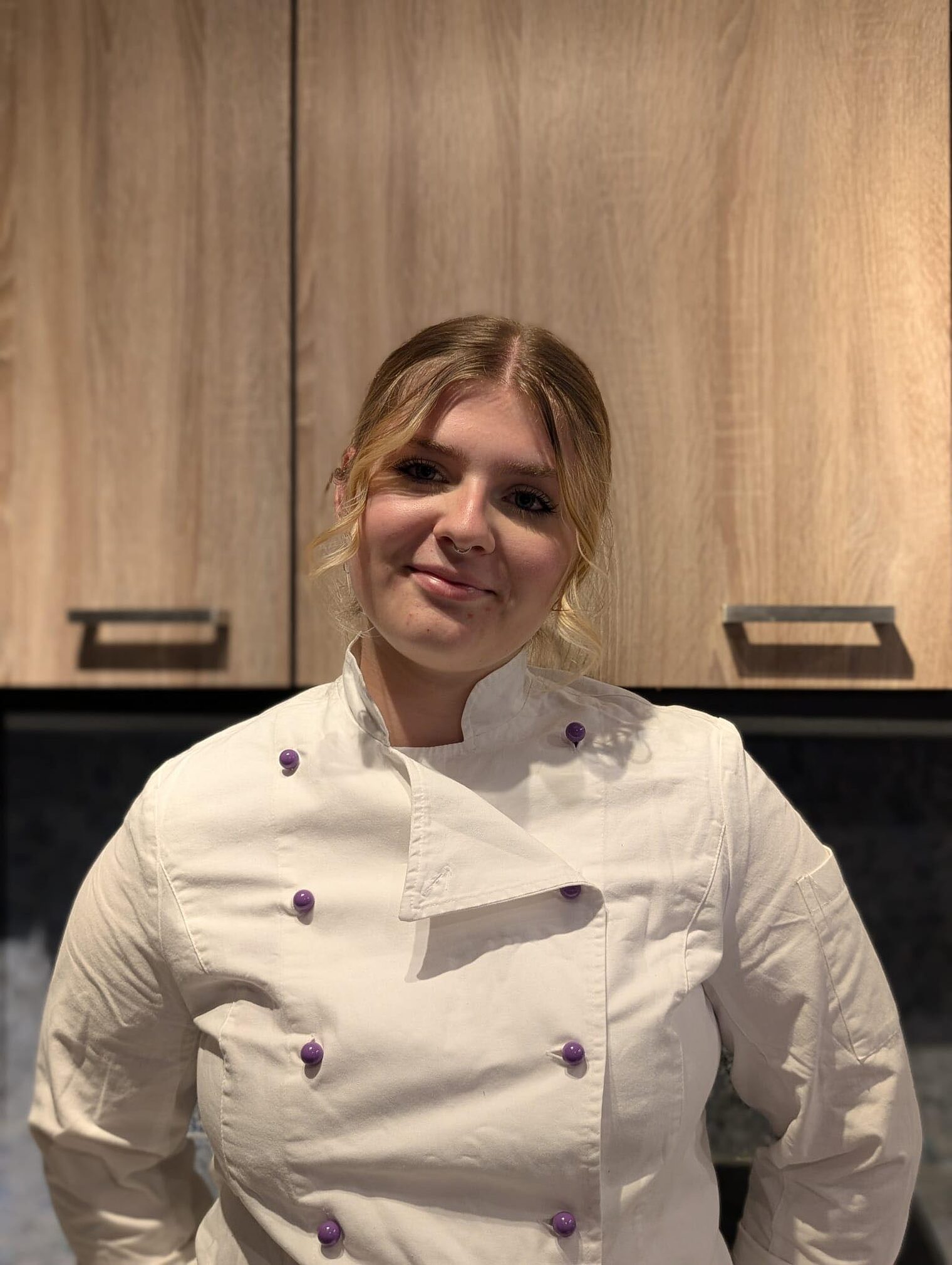 Blonde Frau lächelt in die Kamera, trägt weißes Konditoren-Oberteil Blonde Frau lächelt in die Kamera, trägt weißes Konditoren-Oberteil