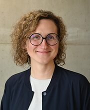 Portrait: Frau mit Locken und runder Brille lächelt in die Kamera