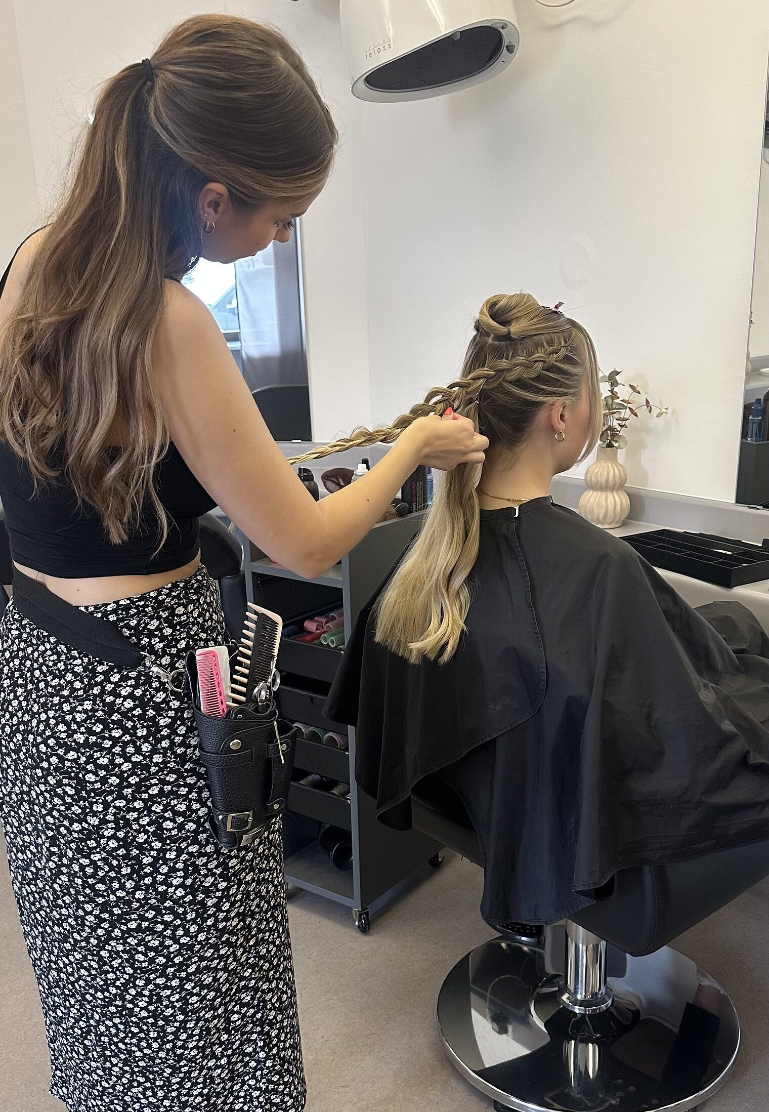 DMH 2025 | Betriebe Friseurin flechtet einer Kundin die langen Haare, Foto aufgenommen von hinten