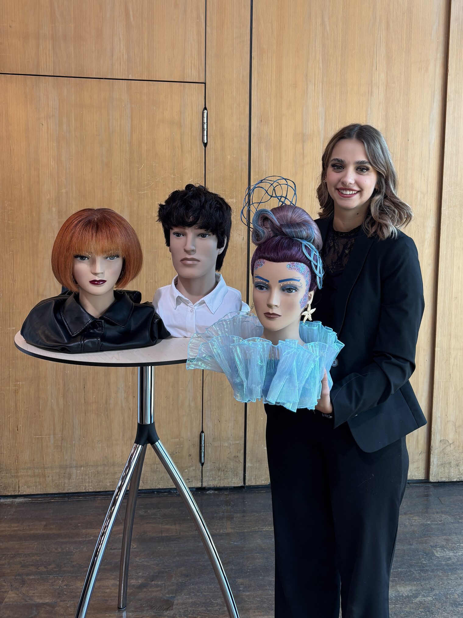 DMH 2025 | Kammersieger Junge Frau steht stolz an einem Stehtisch, darauf drei Frisierköpfe