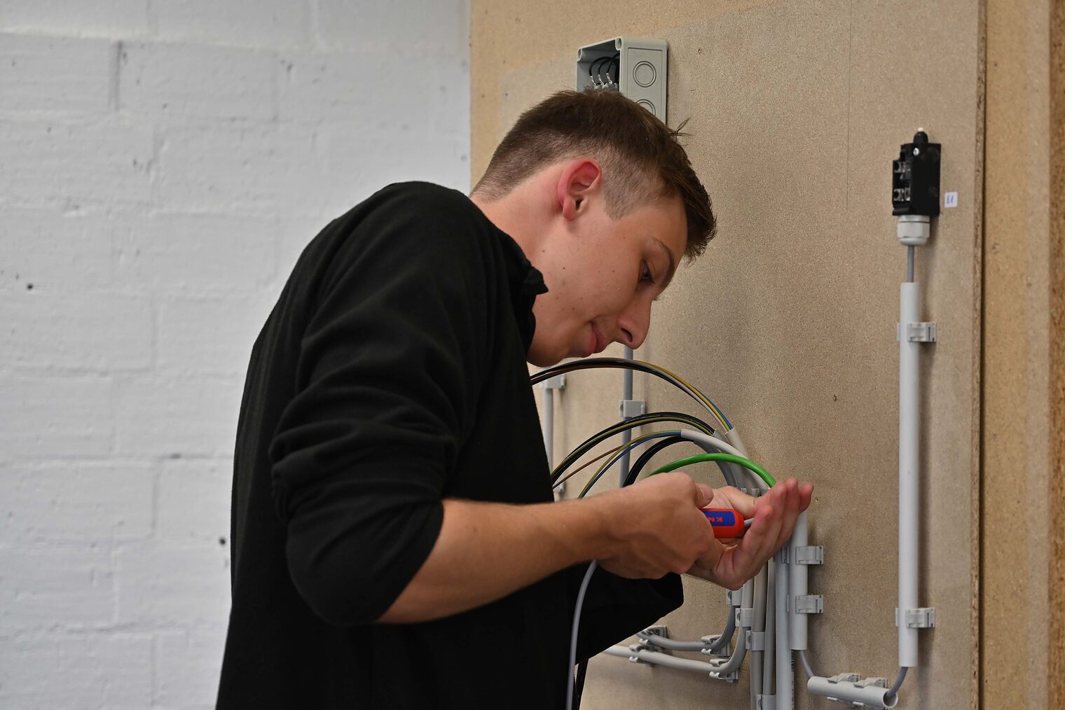 Junger Mann von der Seite, arbeitet an Verkabelung Junger Mann von der Seite, Schraubenzieher in der Hand arbeitet an Verkabelung