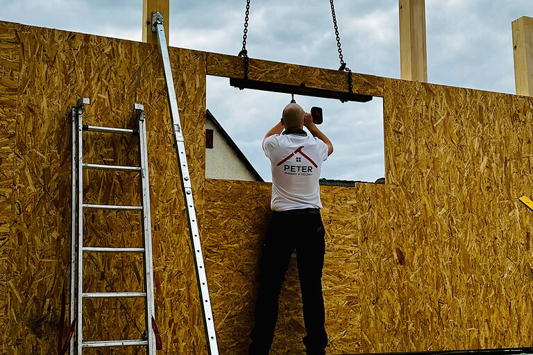 DMH 2025 | Kammersieger Zimmerer auf Baustelle an Holzwand, schreibt auf Plan