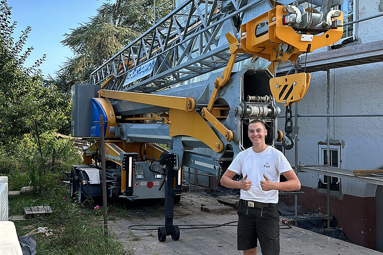 DMH 2025 | Kammersieger Zimmerer vor Baustelle mit Kran, zeigt Daumen hoch