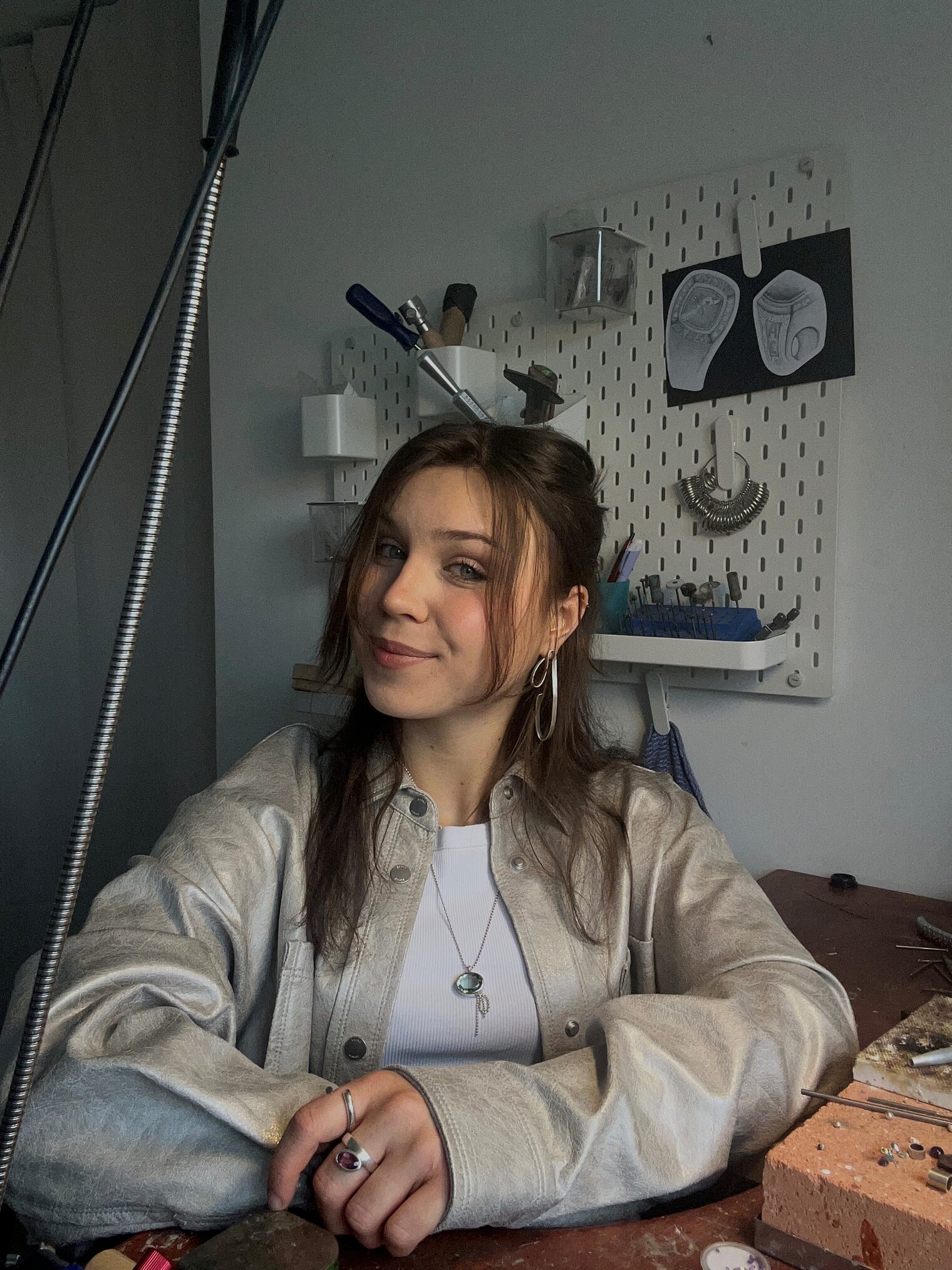 Junge Frau, braune Haare in heller Lederjacke, lächelt in die Kamera Junge Frau, braune Haare in heller Lederjacke, lächelt in die Kamera, Werkstatthintergrund Goldschmiede